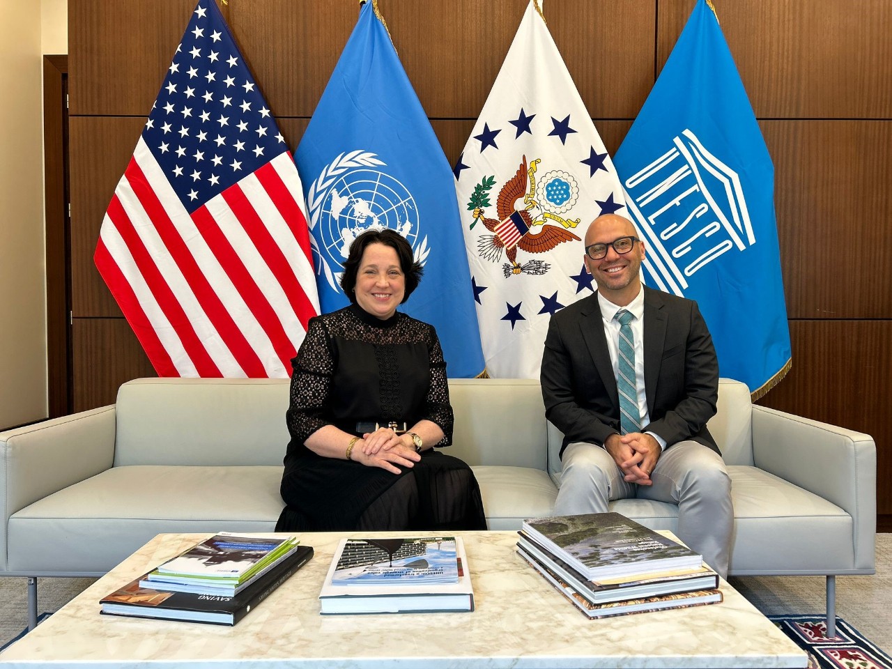 Patrick Ray and U.S. Ambassador Jean Elizabeth Manes sit in front of American and U.N. flags.