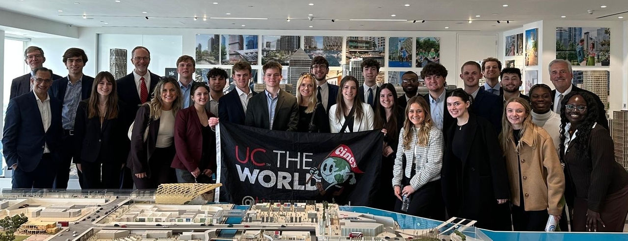 A group of students pose with a UC flag in the Canary Wharf offices