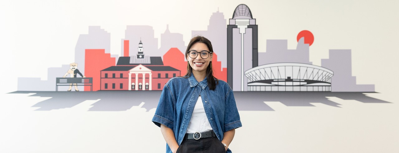 Abigail Miklowski is shown standing in front a mural in a UC dormitory