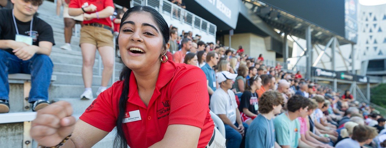 image of UC student orientation leader leading a crowd of hundreds of parents and new students in the university school spirit cheer in Nippert Stadium