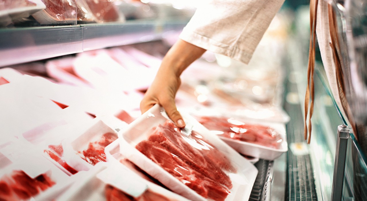 A customer picking up a package of beef in a grocery store.