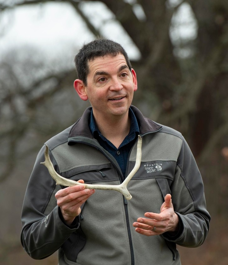 Joshua Miller, PhD, with caribou antlers and environmental portrait outside of the geology building.