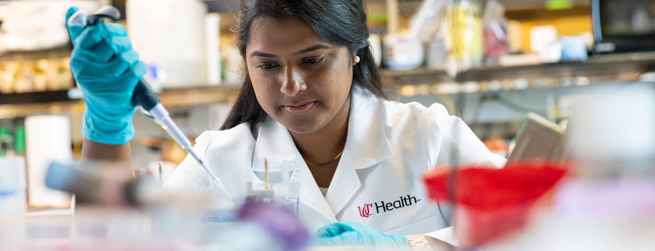 Annabelle Anandappa, wearing a white coat, pipettes a sample at a bench in the laboratory