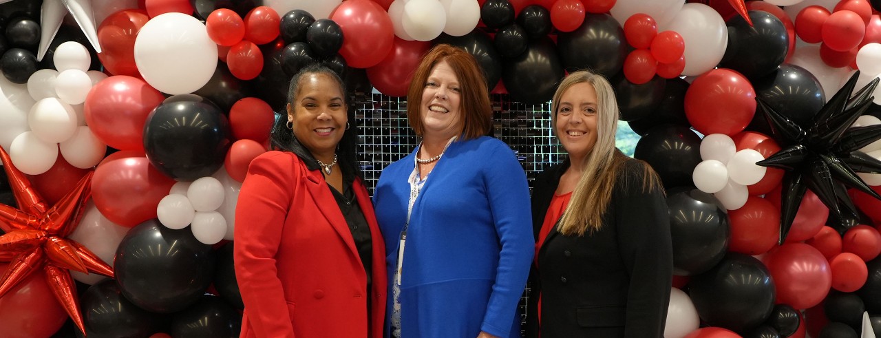Three CPS leaders stand and smile with a balloon background