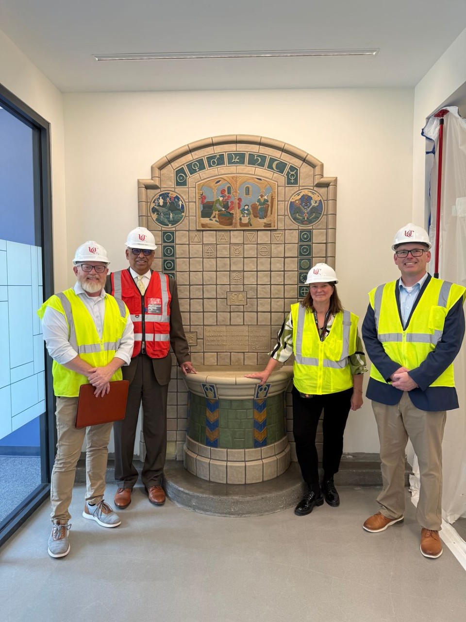 Four people in hardhats and safety vests pose around a fountain.