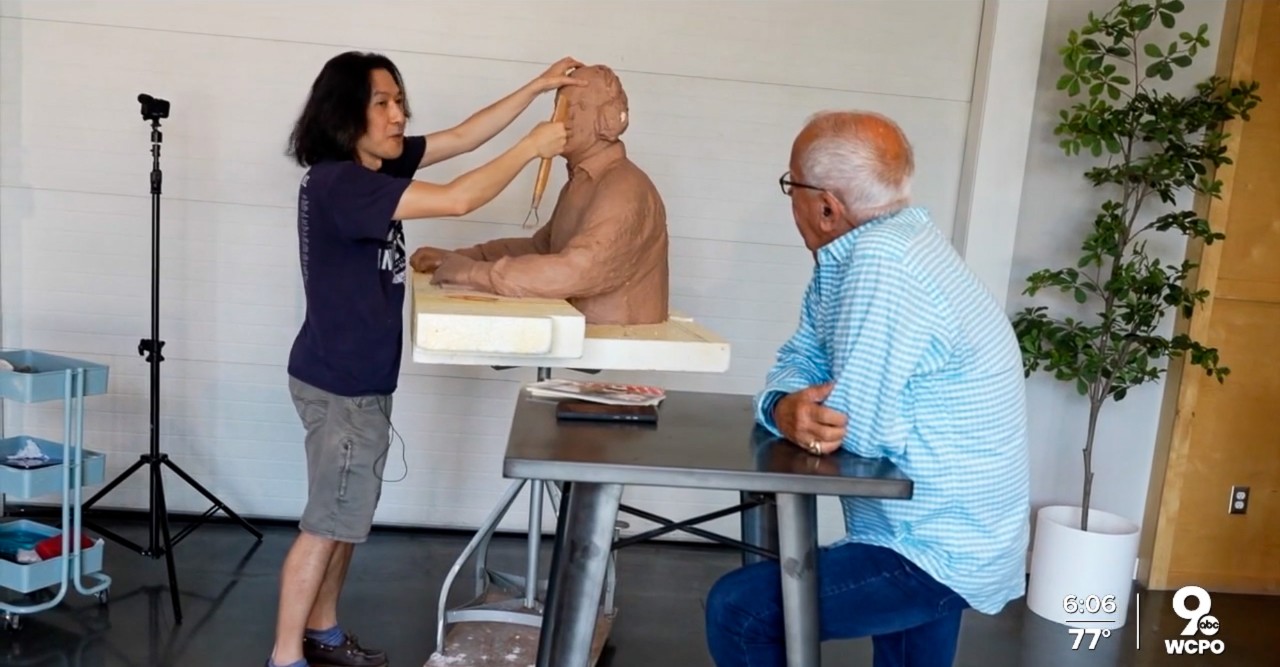Tom Tsuchiya sculpts a clay statue while Marty Brennaman looks on.