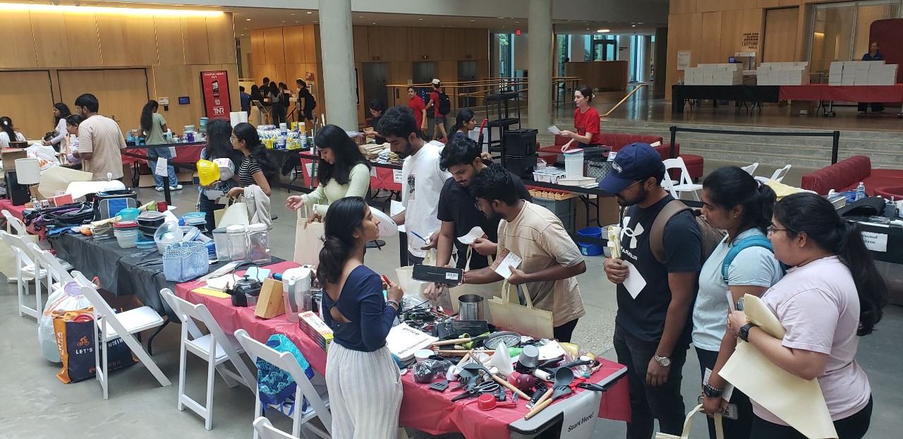 Room full of many students lined up along tables of household items