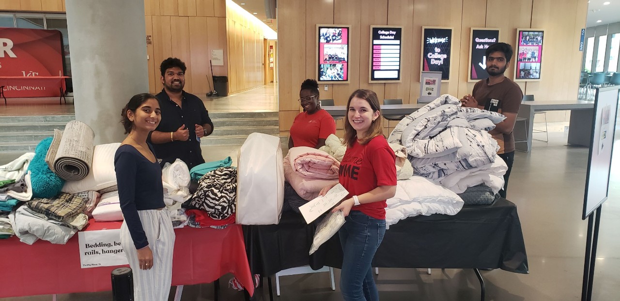 Four volunteers are shown standing near table with piles of bed linen at the Thrifty Move-In event