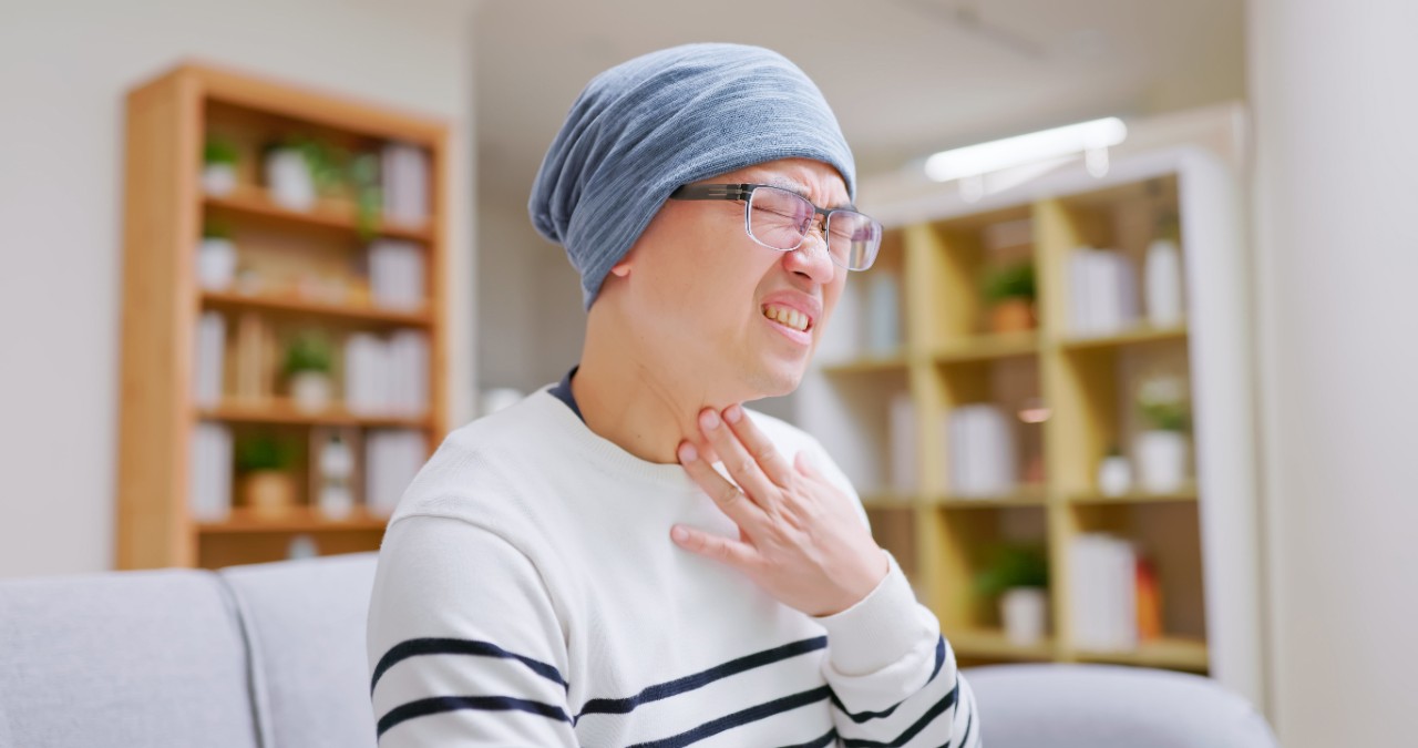 Young man holds hand to throat and appears to be in pain