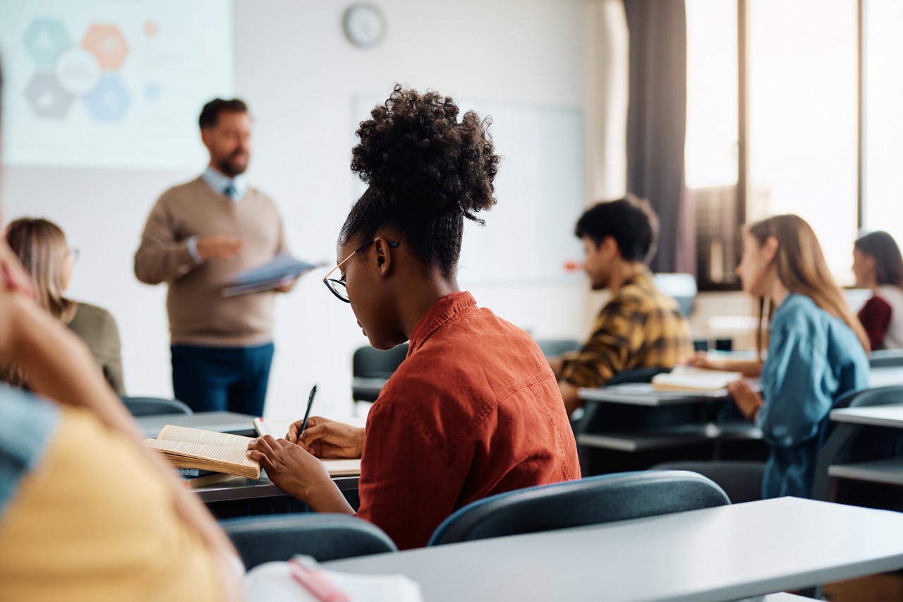 A young woman takes notes in a college classroom