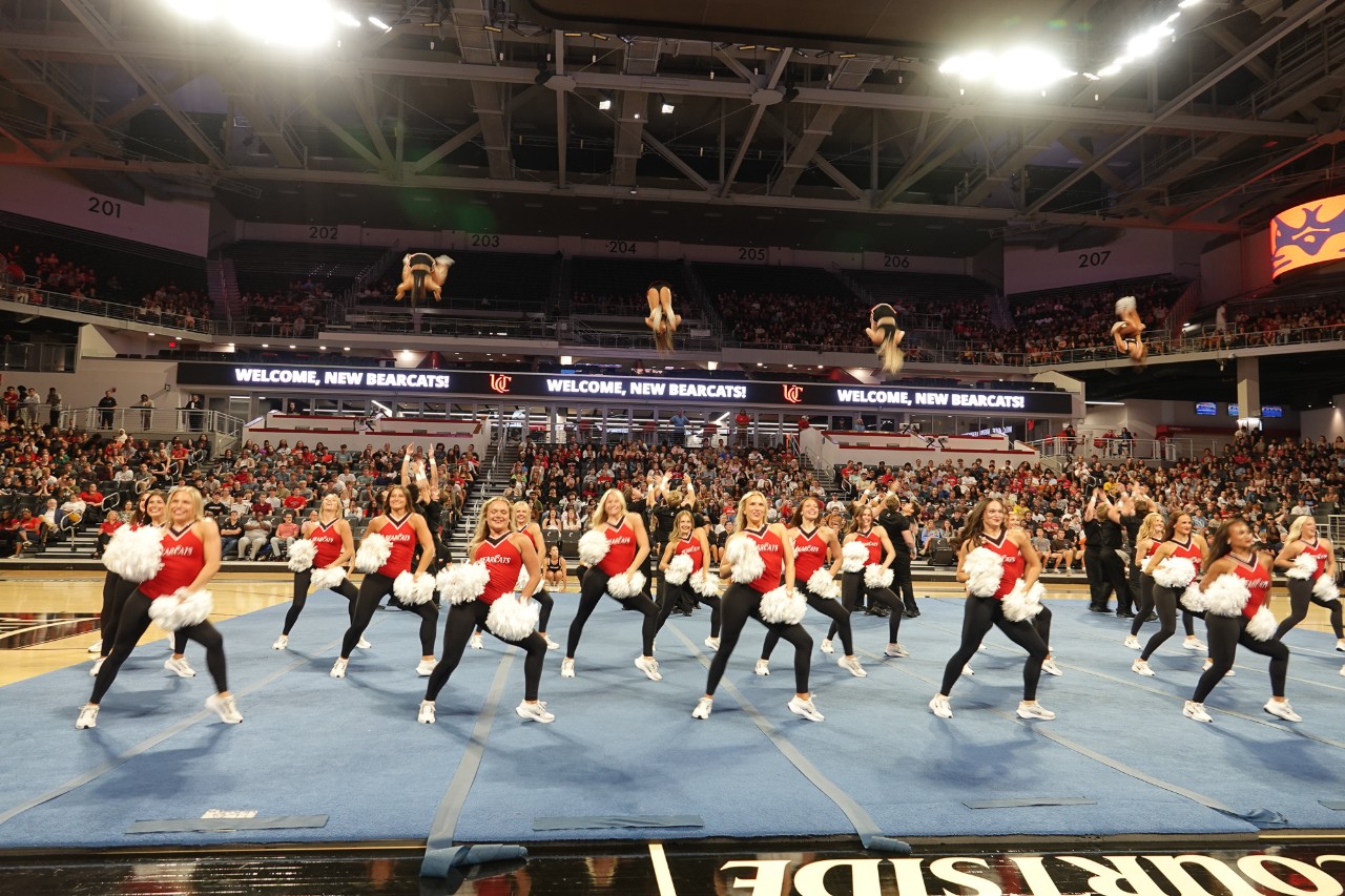 More than a dozen cheerleaders with pompoms perform before hundreds of new UC students inside Fifth Third Arena