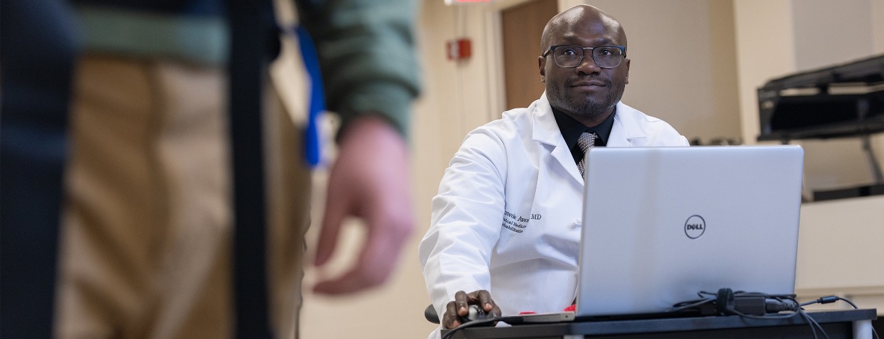 Dr. Awosika sits at a laptop observing a person standing in the posturography machine
