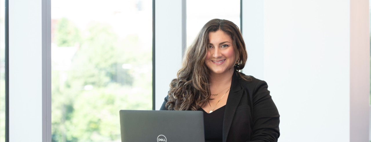 Alique Topalian sits at a table in front of a laptop and smiles