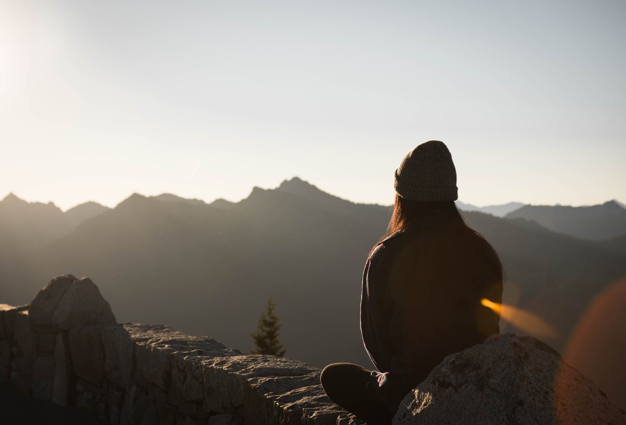 Sun coming up over mountainside as person looks on, representing mindfulness, well-being and mental health
