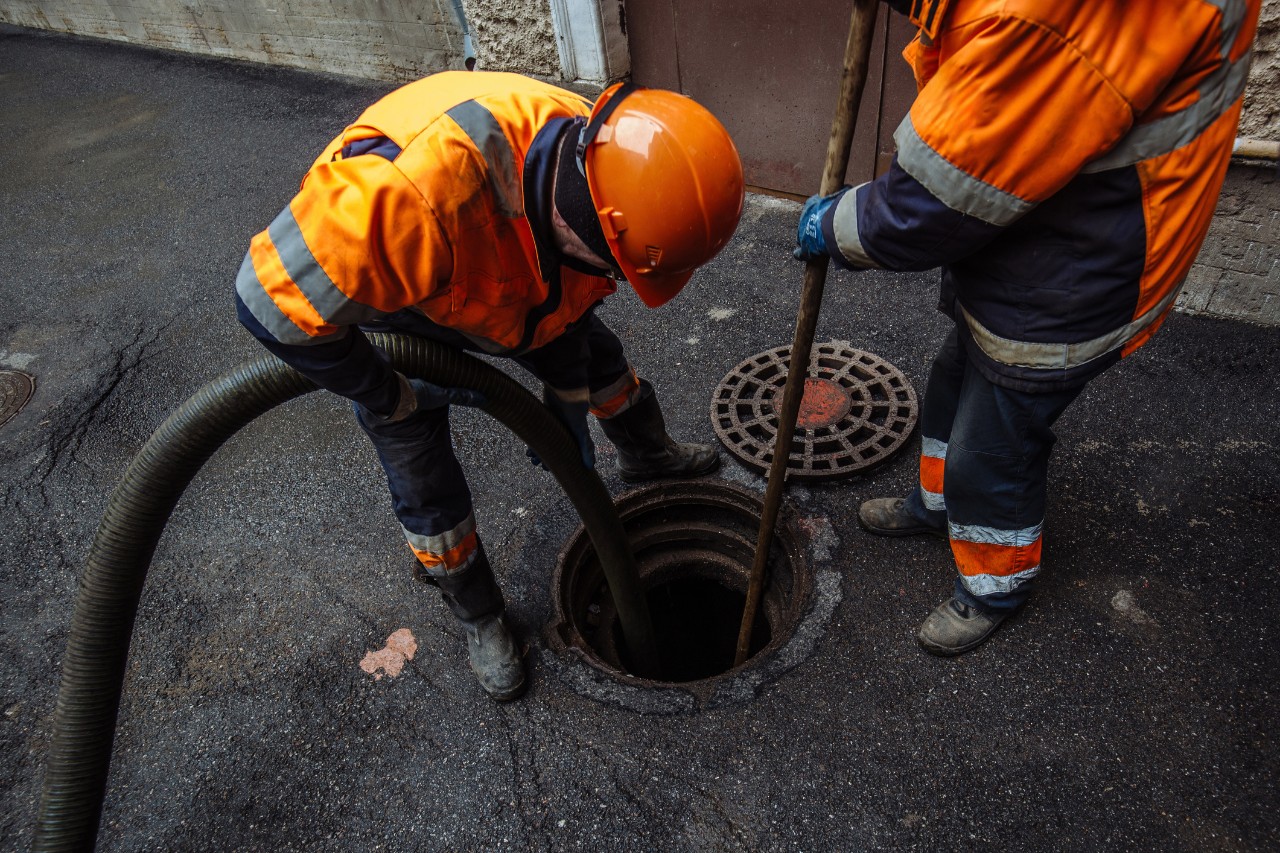 Sanitation workers over an open manhole.