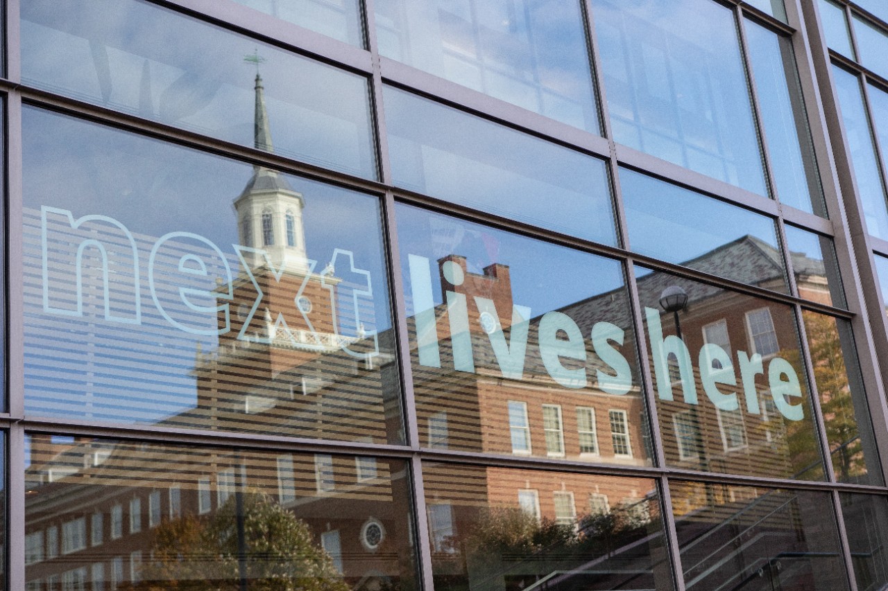 UC's campus reflected through a window with a "next lives here" decal. 
