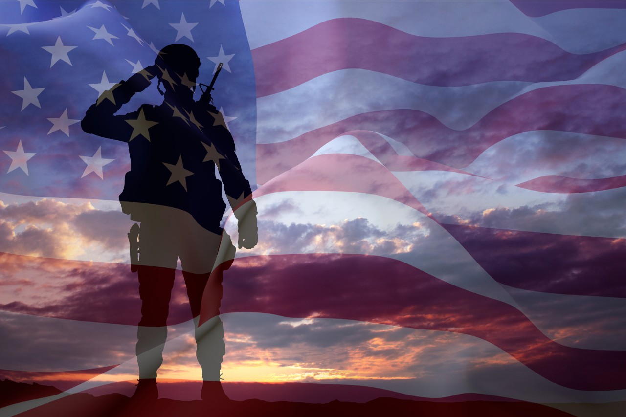 Soldier standing on ground saluting to an American flag in the sky 