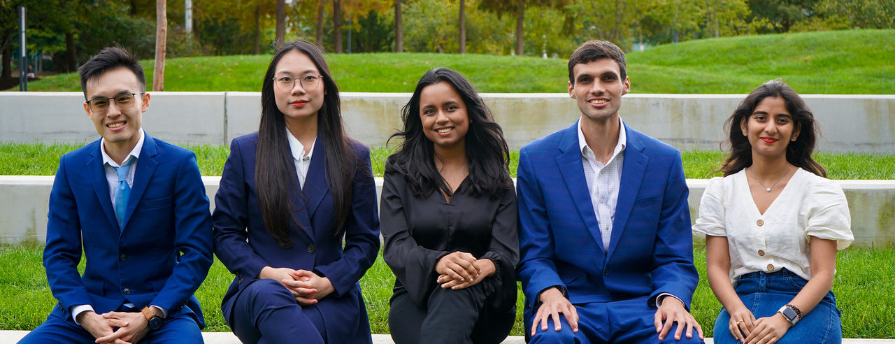 international students pose sitting on a wall, wearing business casual attire