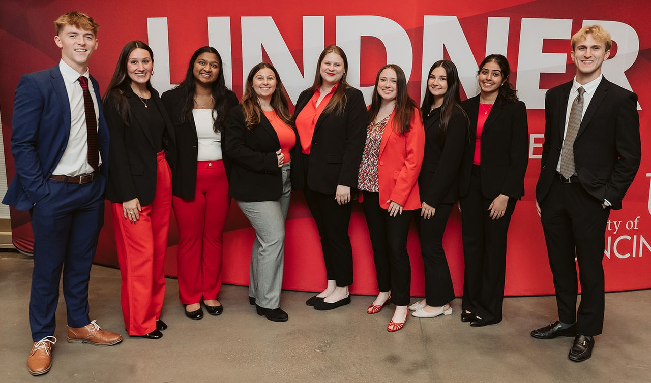 Students in red and black and blue professional dress stand in front of a red banner.
