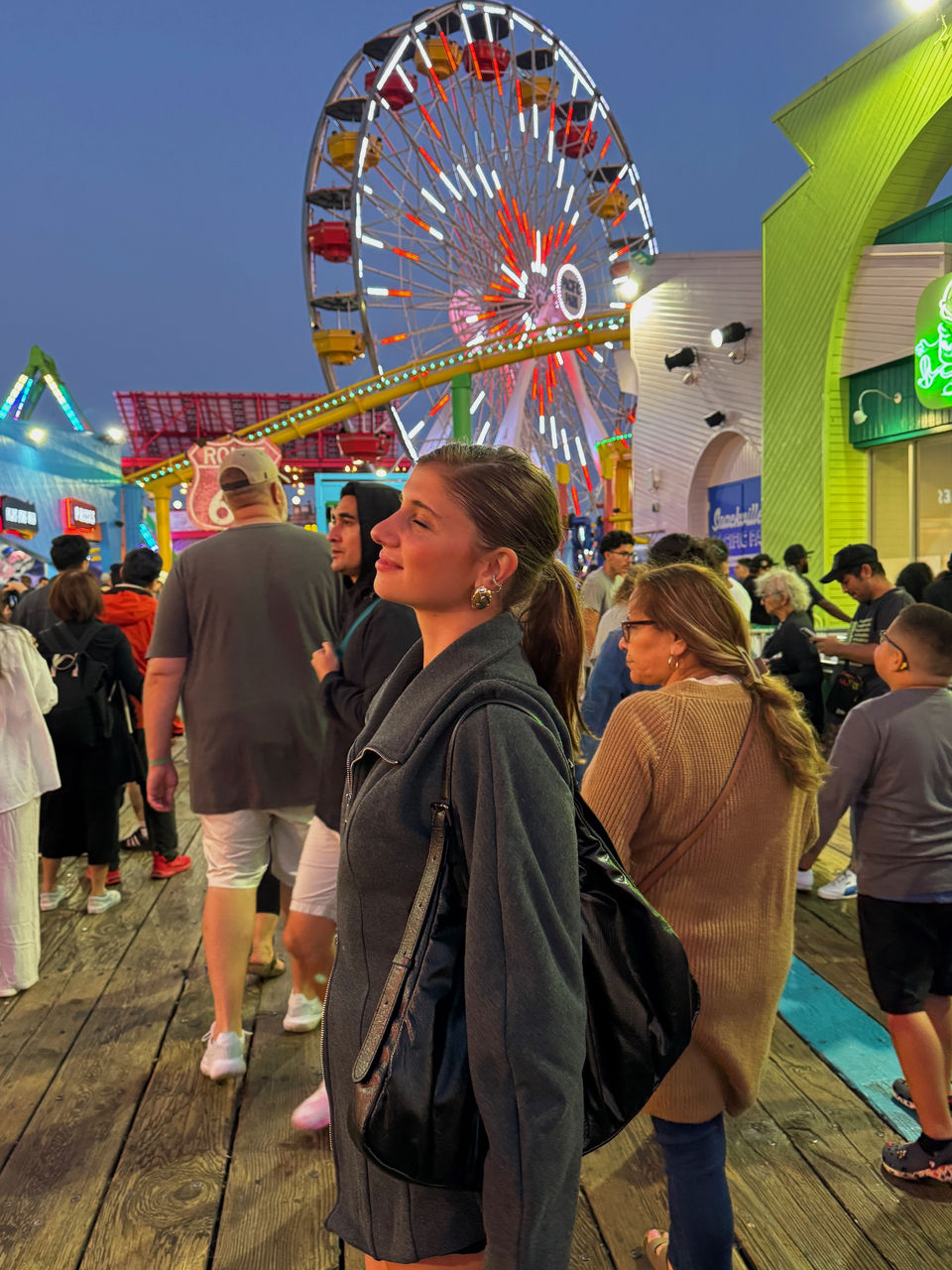 Delfina Lassalle standing on a pier, at night in Santa Monica, California, with a ferris wheel in the background. 