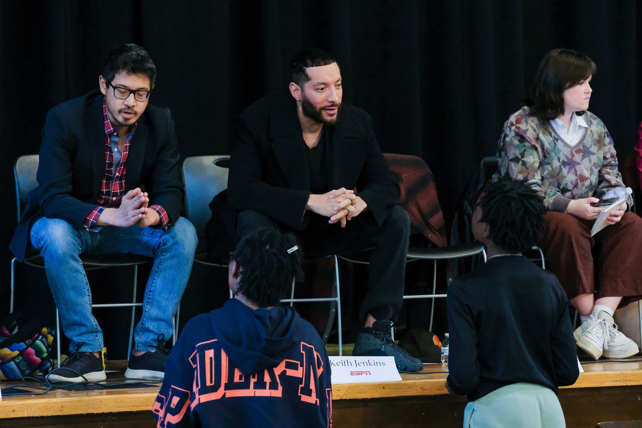 Three people on stage talk to students. 