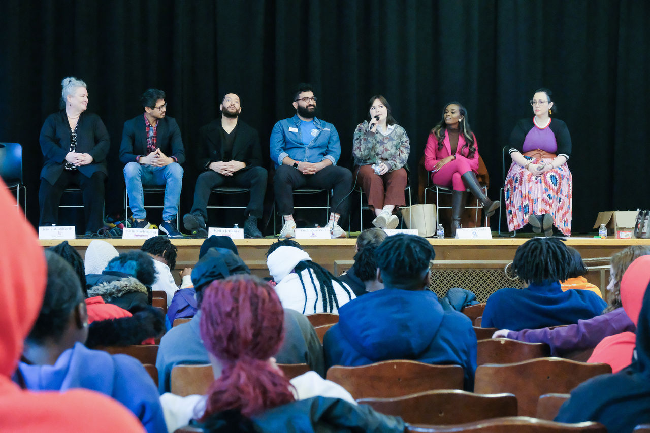 Panelists sit on stage in front of an auditorium of students.