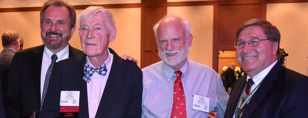 Four men in suits, smiling.