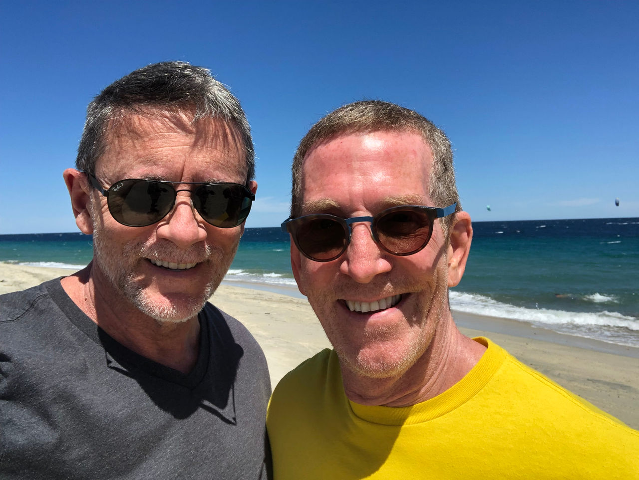 Two men smiling on a beach.