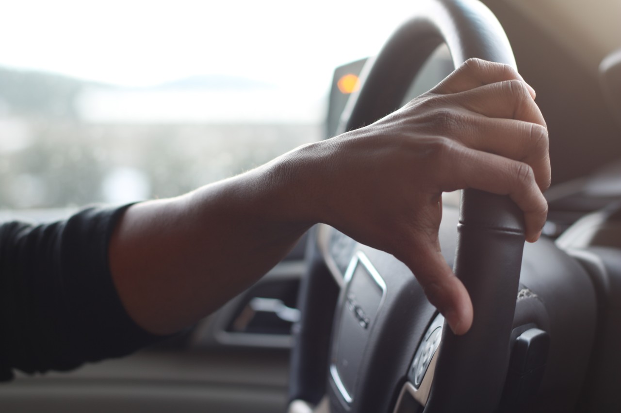 Driver's hand on the steering wheel of a car.