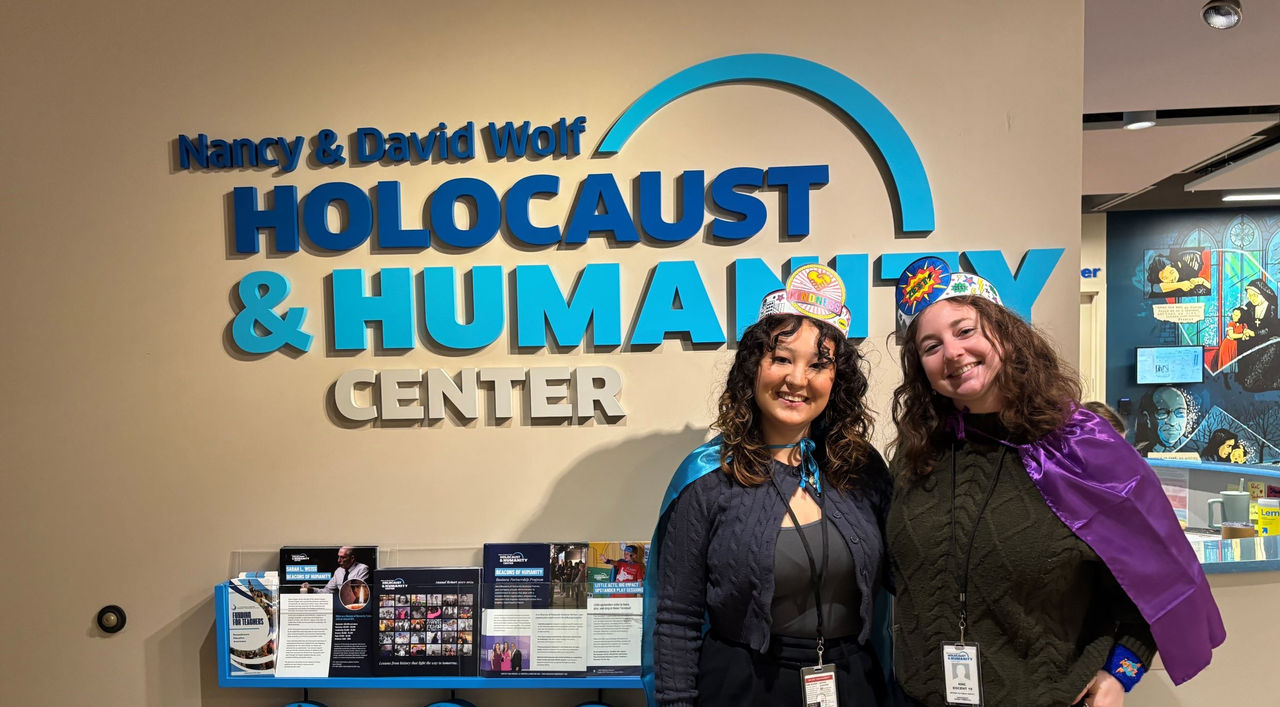 UC students wearing crowns in front of the Nancy & David Wolf Holocaust & Humanity Center sign
