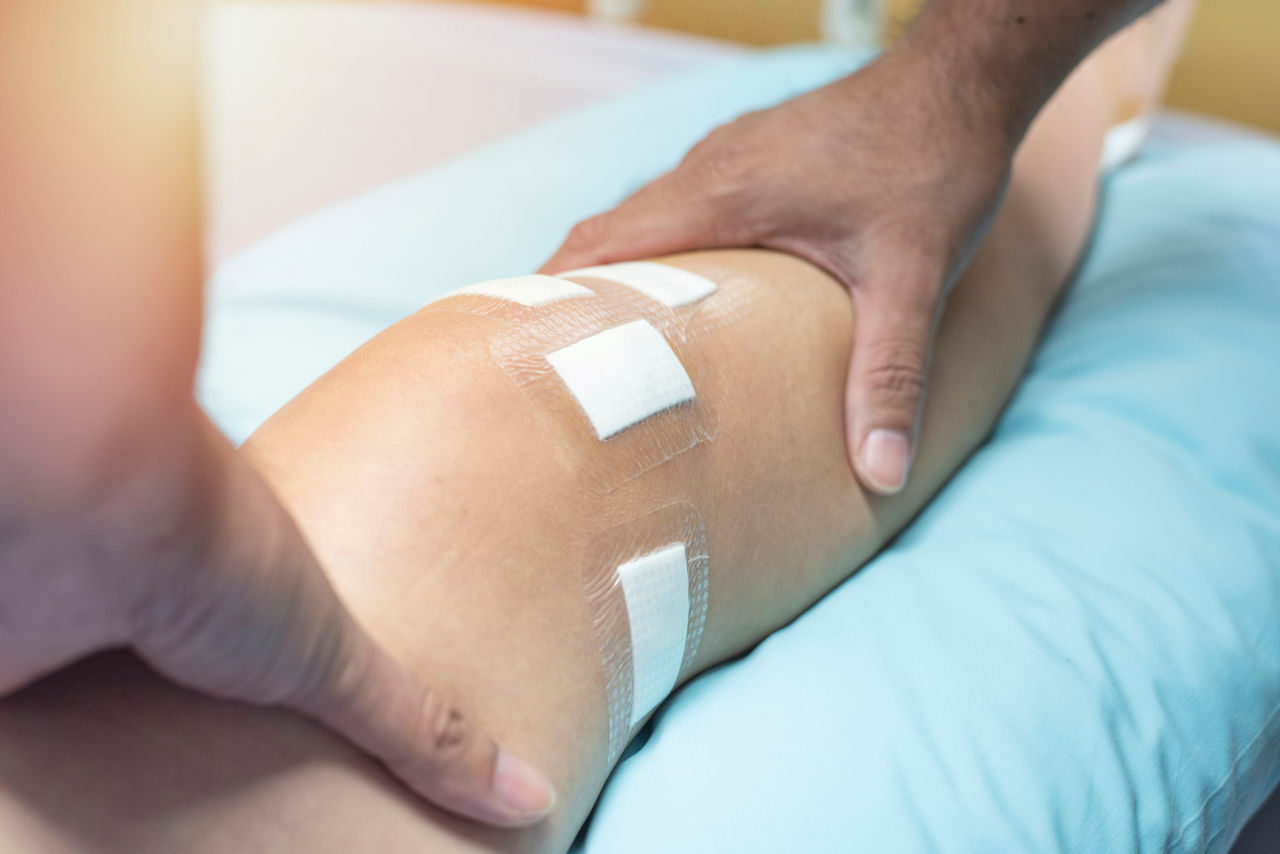 A health care provider's hands on a person's leg with bandages around the knee