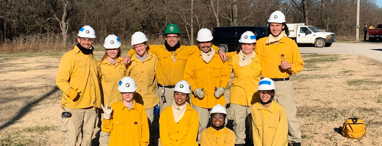 A group of people wearing yellow hard hats, engaged in a construction or safety-related activity outdoors.  