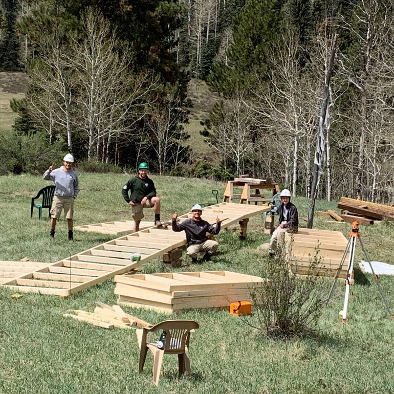 A group of people collaborating on the construction of a wooden structure outdoors. 