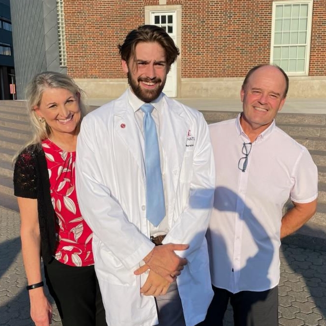 Kaleb Kiely wearing a white coat between his parents