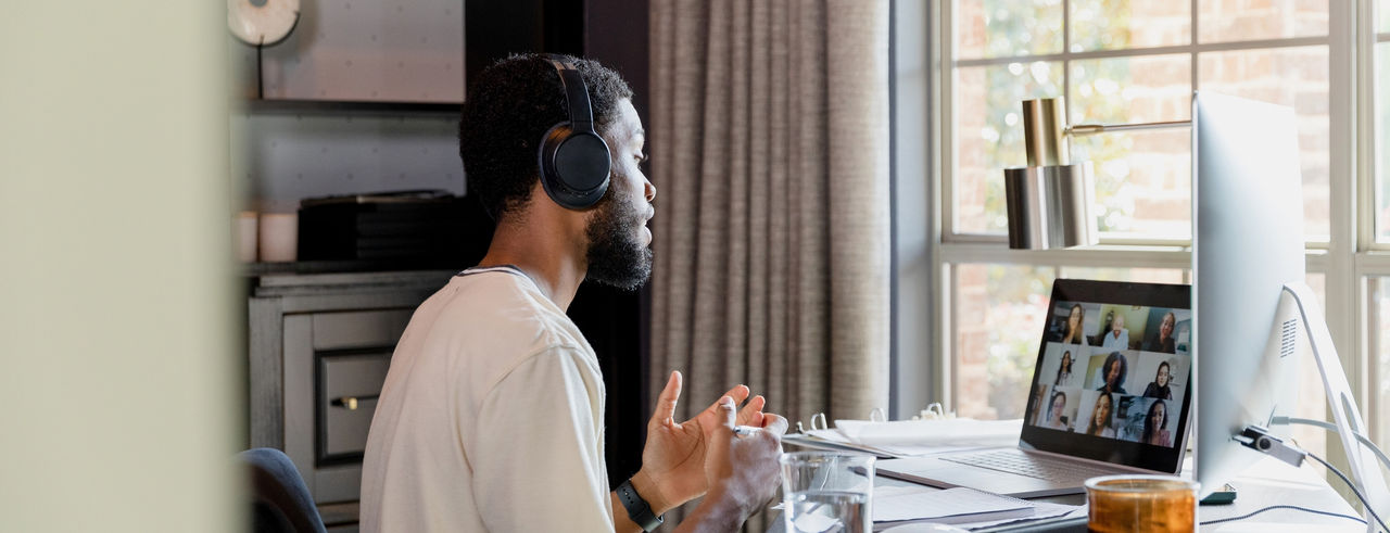 A man sits at a desk wearing headphones and talking to a virtual support group on his laptop
