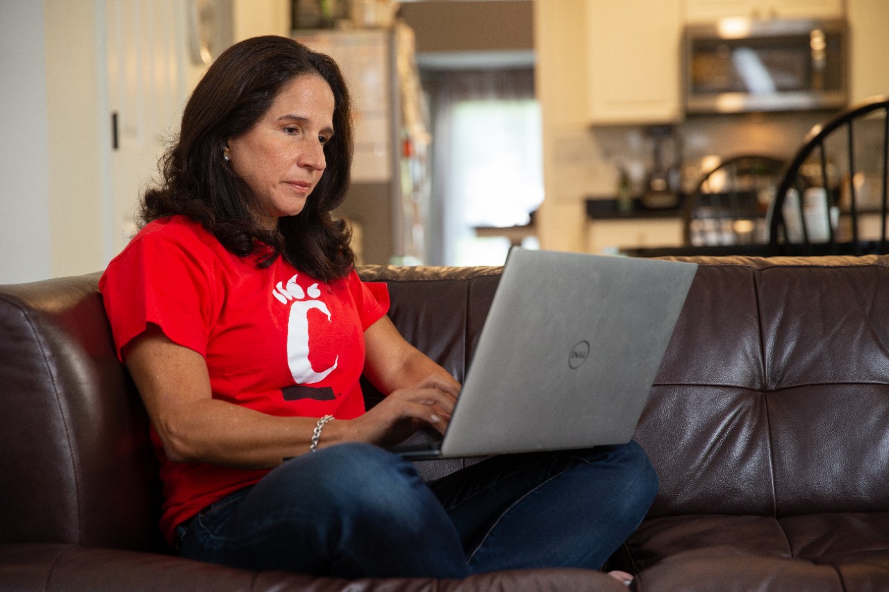 A woman wearing a UC shirt sits on a couch with her laptop.
