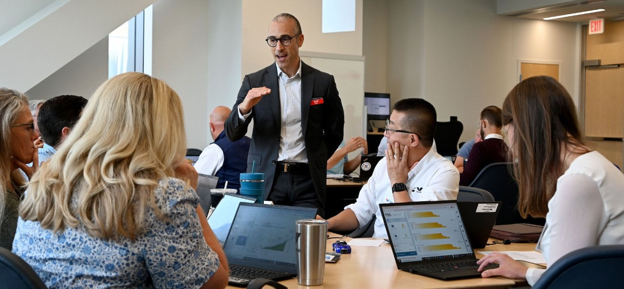 Man speaking to a group of three at desks.