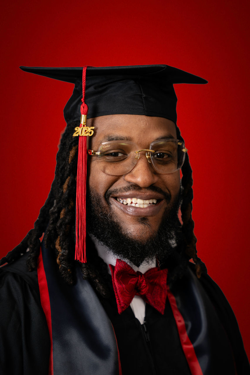 Nick Baynes in cap and gown smiling against a red background.