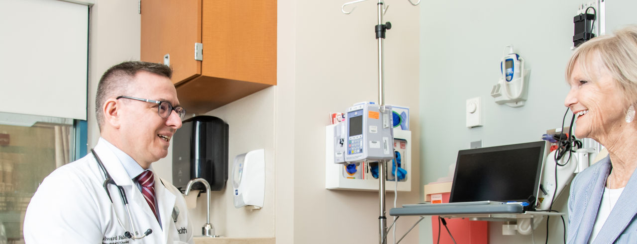 Ed Faber wears a white coat and speaks with a female patient in an exam room