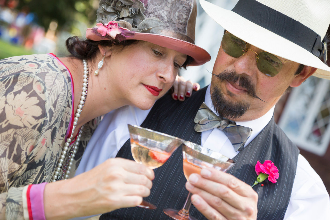 Woman and man dressed in prohibition era clothing enjoy a toss of alcohol