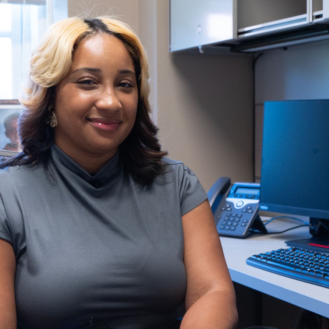 Jordyn Freeman smiles as she sits in her office with a computer beside her