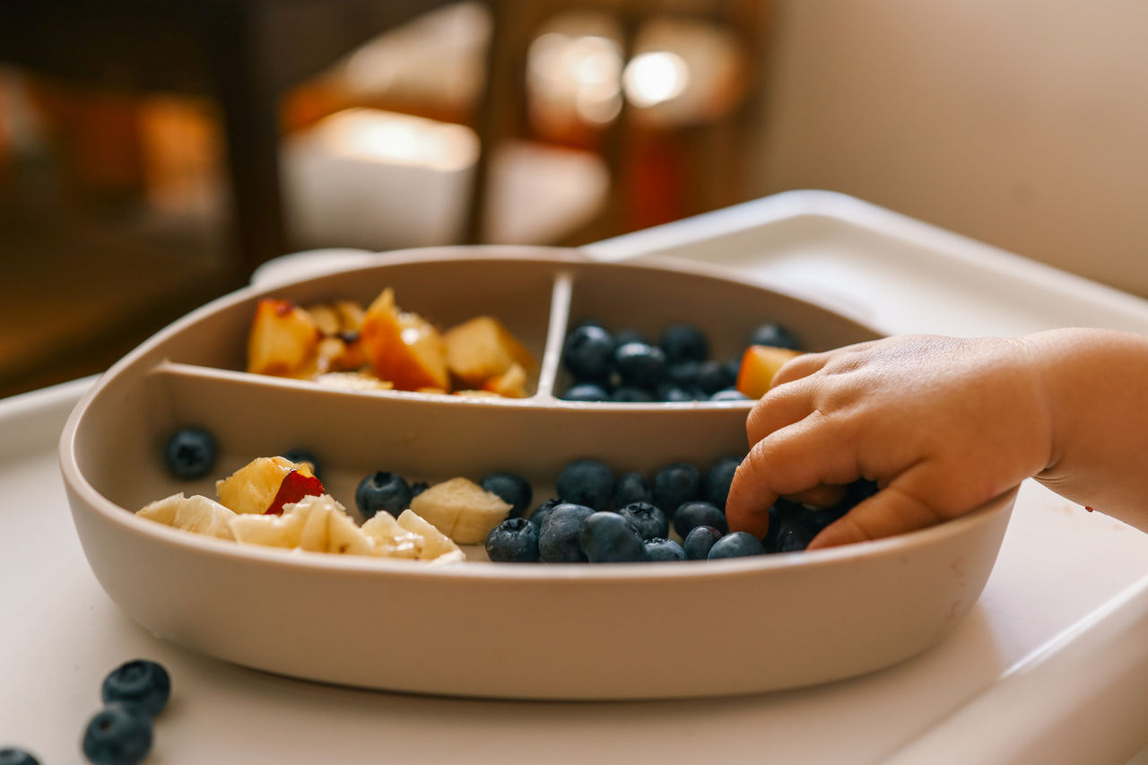 infant hand dipping into a plate with berries