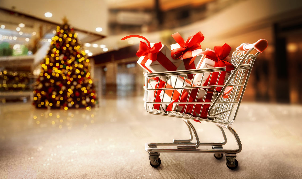 A shopping cart full of gifts in front of a Christmas tree.
