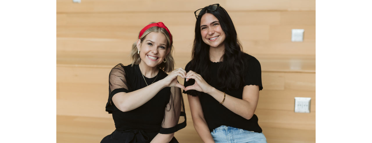 Two students smiling with their hands making a heart