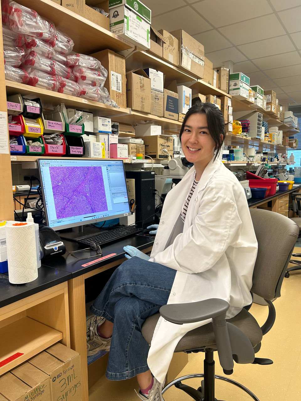 Sakura Adachi smiles next to a photo of cell staining on a computer at the Miethke Lab. 