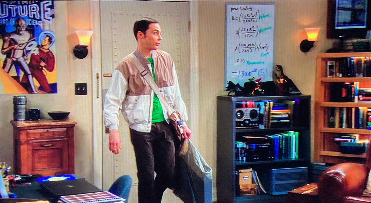 A screenshot from the TV show Big Bang Theory features character Sheldon Cooper walking past a whiteboard with an equation and a frowny face.