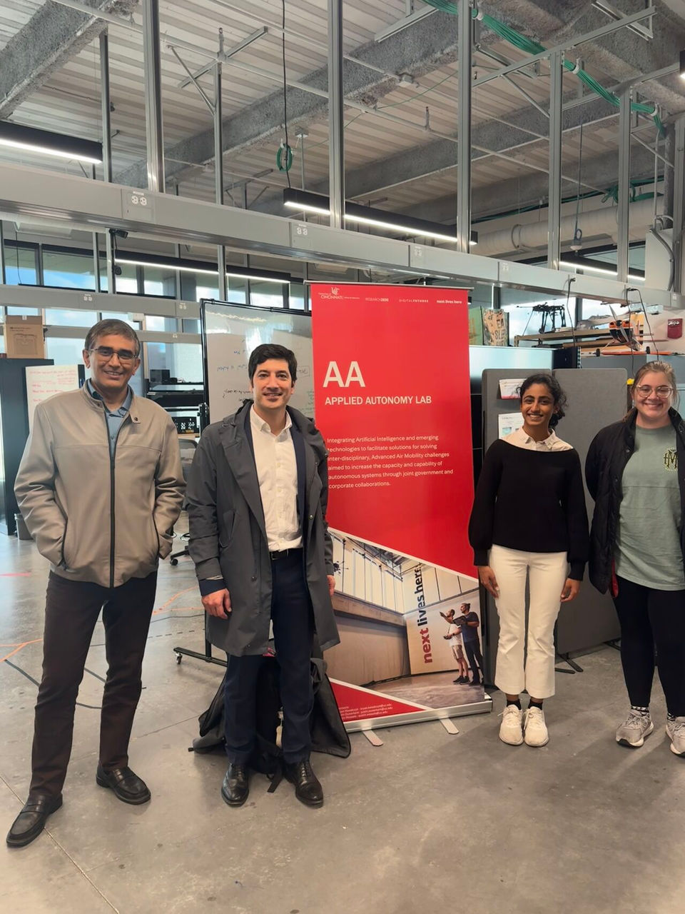 Prissha Chawla stands with her mentors in front of a UC autonomy lab sign 