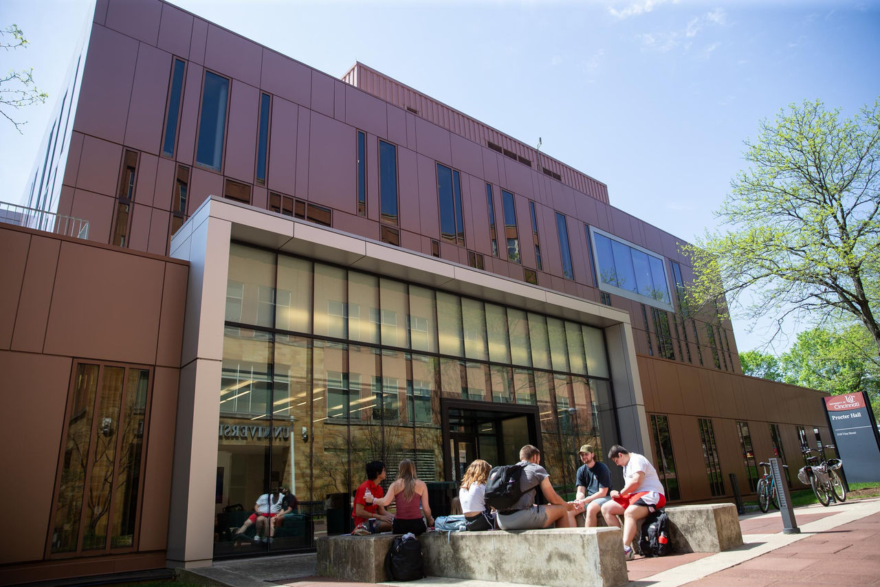Exterior image of the UC College of Nursing, Procter Hall, with students sitting in front of the building
