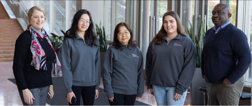 Five people pose in a row for a group photo.