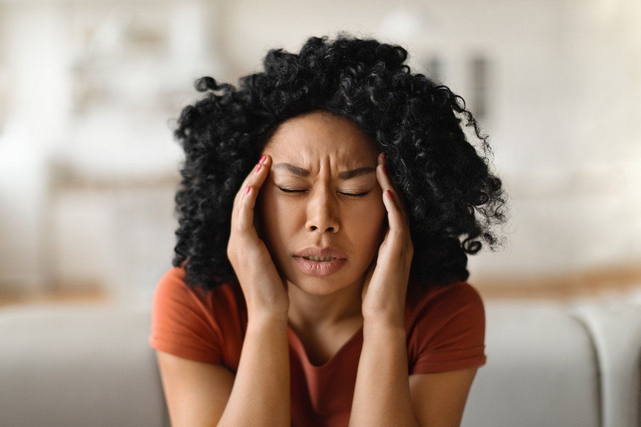 A woman in pain holds the sides of her head with her hands